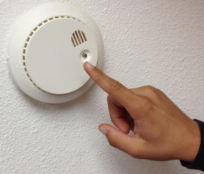 Smoke Alarm Being Checked by white hand against grey background.